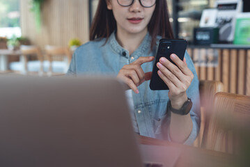 Wall Mural - Young asian woman using mobile phone with laptop computer on table at coffee shop. Woman using smartphone for online shopping, mobile banking via mobile app, modern people lifestyle