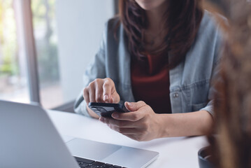 Wall Mural - Asian business woman using mobile phone with laptop computer on table. Woman surfing the internet, searching the information on smartphone during working on laptop computer at home office