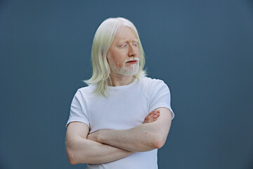 elderly man with long white hair and beard, thoughtful expression, arms crossed, gray background, casual white t shirt, studio shot, portrait photo capturing wisdom and introspection