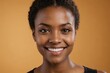 © ThomasLENNE - Full framed very close face portrait of a smiling young black woman with amber eyes looking at the camera, studio shot,amber background.