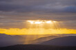 © Austockphoto - Distant view of golden rays of sunlight over a mountain range