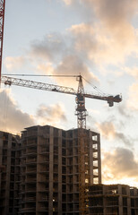 Poster - Cranes are positioned at a construction site, silhouetted against a colorful sunset with clouds scattered in the sky
