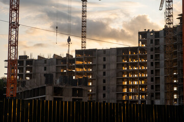 Leinwandbilder - Cranes operate at dusk, lifting materials above a bustling construction site as concrete structures take shape