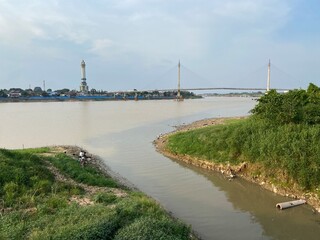 Jambi, Indonesia - August 27th 2024: Batanghari River in the afternoon with the backdrop of the Gentala Arasy pedestrian bridge and cloudy skies