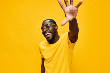 Smiling young Black man wearing yellow shirt and glasses against a bright yellow background expressing joy and enthusiasm, ideal for concepts of happiness and positivity