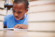 © STEEXBuyout/peopleimages.com - Black child, writing and study in library for education, knowledge or academic opportunity at elementary school. Young boy, learning or books on table for lesson, growth and progress in assessment