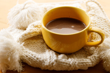 Cup of delicious hot chocolate on warm sweater on wooden table background. Selective focus.