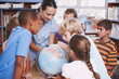 © STEEXBuyout/peopleimages.com - Children, teacher and map with globe in library for geography education, planet learning and and science. Students, woman and global teaching with earth atlas for spatial discussion of climate change
