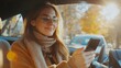 © Oleksandr Kozak - Happy woman in the car in the driver's seat looks at the smartphone. A young woman uses a mobile phone to navigate in the city, pay for parking. Business, technology concept.