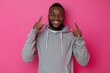 © Minerva Studio - Cheerful young man in a hoodie pointing upwards with both hands on a vibrant pink backdrop