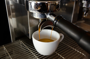 Closeup shot of an espresso maker pouring coffee into a cup inside of a cafe.