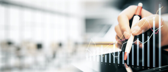 Poster - Businessman's hand holding a pen with financial graph overlay, in a blurred office background.