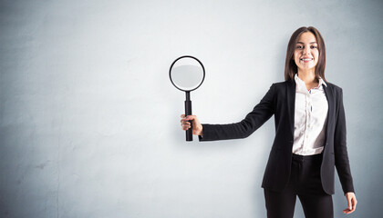 Businesswoman holding magnifying glass against a wall background.