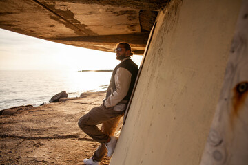 portrait of a handsome and sporty young guy dressed in casual clothes in a seaside location. The model is posing with a smiling expression while standing on a beach at sunset