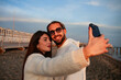 © Raffaele Conti RC88 - close-up of a young and charming couple of lovers taking a selfie with their smartphones while they are on the beach at sunset. The two lovers are accomplices and in love with each other.