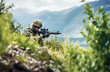 © bborriss - The  army soldier shoots from a sniper rifle, hidden behind a bush on a hilltop