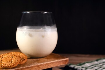 A glass of cold milk and cookies on wooden table on a dark background