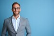 © pham - A smiling young man in a suit stands confidently in front of a bright blue background, showcasing a professional appearance