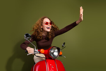 Poster - Photo of adorable lovely girl wear brown shirt riding moped waving arm empty space isolated khaki color background