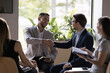 © fizkes - Happy confident handsome businessmen shaking hands on meeting with colleagues sitting in circle. Boss, project leader thanking employee for idea, giving handshake with respect