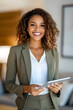 © Tanya - Smiling African real estate agent in olive green suit with a digital tablet in a stylish and modern living room environment.