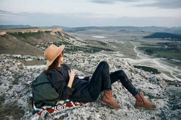 Serene woman with backpack and hat sitting on rock gazes out over picturesque valley