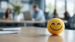 © Pinklife - A cheerful yellow smiley stress ball is prominently placed on a wooden desk, set against a blurred backdrop of an office environment, promoting calm and positivity among employees.