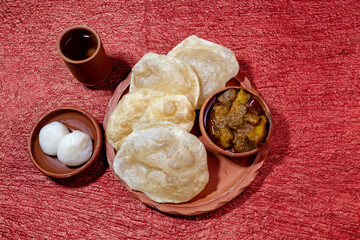 Bengali traditional and most common breakfast or snack 'Luchi' or 'Poori' or deep-fried flatbread. Served with spicy potato curry and indian dessert rosogolla in earthenware