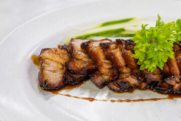 A close-up view of delicious char siu served on a plate alongside fresh cucumber slices.