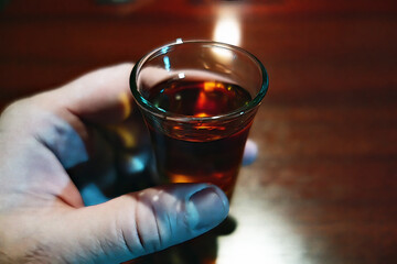 A hand holds a glass of alcohol near a candle during Christmas h