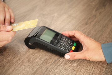 Canvas Print - Woman taking payment from client via credit card terminal at wooden table, closeup