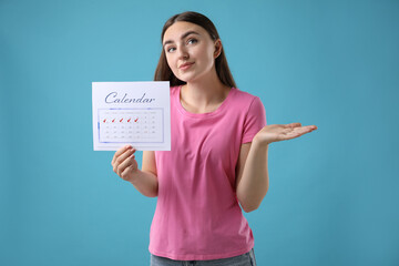 Poster - Woman holding calendar with marked menstrual cycle days on light blue background