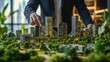 © B 7 YOU - Close-up of a businessman's hand pointing at a model city with tall skyscrapers and lush greenery.