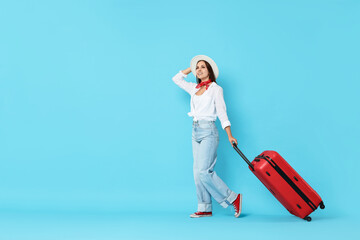 Canvas Print - Happy young woman with suitcase on light blue background, space for text