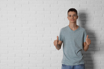 Poster - Teenage boy wearing grey t-shirt and showing thumbs up near white brick wall, space for text