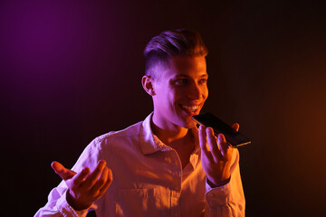 Poster - Young man recording voice message via smartphone on dark background with neon lights