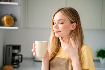 Photo of attractive teen woman drink coffee smell aroma dressed apron enjoy preparing delicious food kitchen indoors