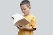 © Stella - A six year old Asian little boy in a yellow shirt holding book isolated on gray background. Young student kid enjoys reading. Portrait child with school book. Education of kid concept.
