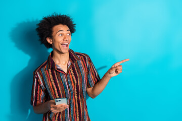 Poster - Portrait of nice young man hold phone indicate finger empty space wear shirt isolated on turquoise color background