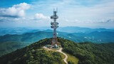 A tall telecommunications tower stands atop a green mountain, surrounded by scenic hills and a blue sky with scattered clouds, emphasizing modern connectivity in nature.