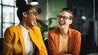 © Iona - Two women in business attire share a hearty laugh in a modern office, radiating positivity and camaraderie.