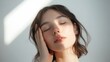 © Danudet.C - Woman shoulder-length portrait with her hand on her face, eyes shut, soft studio lights, minimal white background, radiant skin