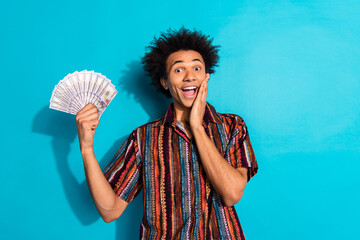 Canvas Print - Portrait of young businessman wavy hair wearing summer shirt holding his first million dollars shocked isolated on aquamarine color background