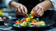 © Oksana - A culinary student decorates a dish with fresh flowers and vegetables on a black plate in a professional kitchen