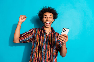 Canvas Print - Portrait of nice young man raise fist hold phone wear shirt isolated on turquoise color background