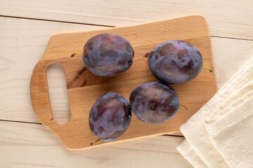 Wall Mural - Ripe plums with wooden cutting board on wooden table, macro, top view.