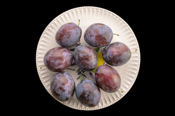 Wall Mural - Sweet plums in a ceramic plate on a black background, macro, top view.