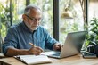 © Artem Zatsepilin - senior man sitting at desk with laptop, participating in online class, with notebook and pen ready for taking notes
