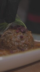 Wall Mural - Vertical slow-motion footage of adding herb on a delicious meat ball in sauce served in white plate