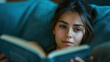 © RISHAD - Young woman relaxing on a couch, deeply engaged in reading a book, with soft lighting creating a cozy and introspective atmosphere.